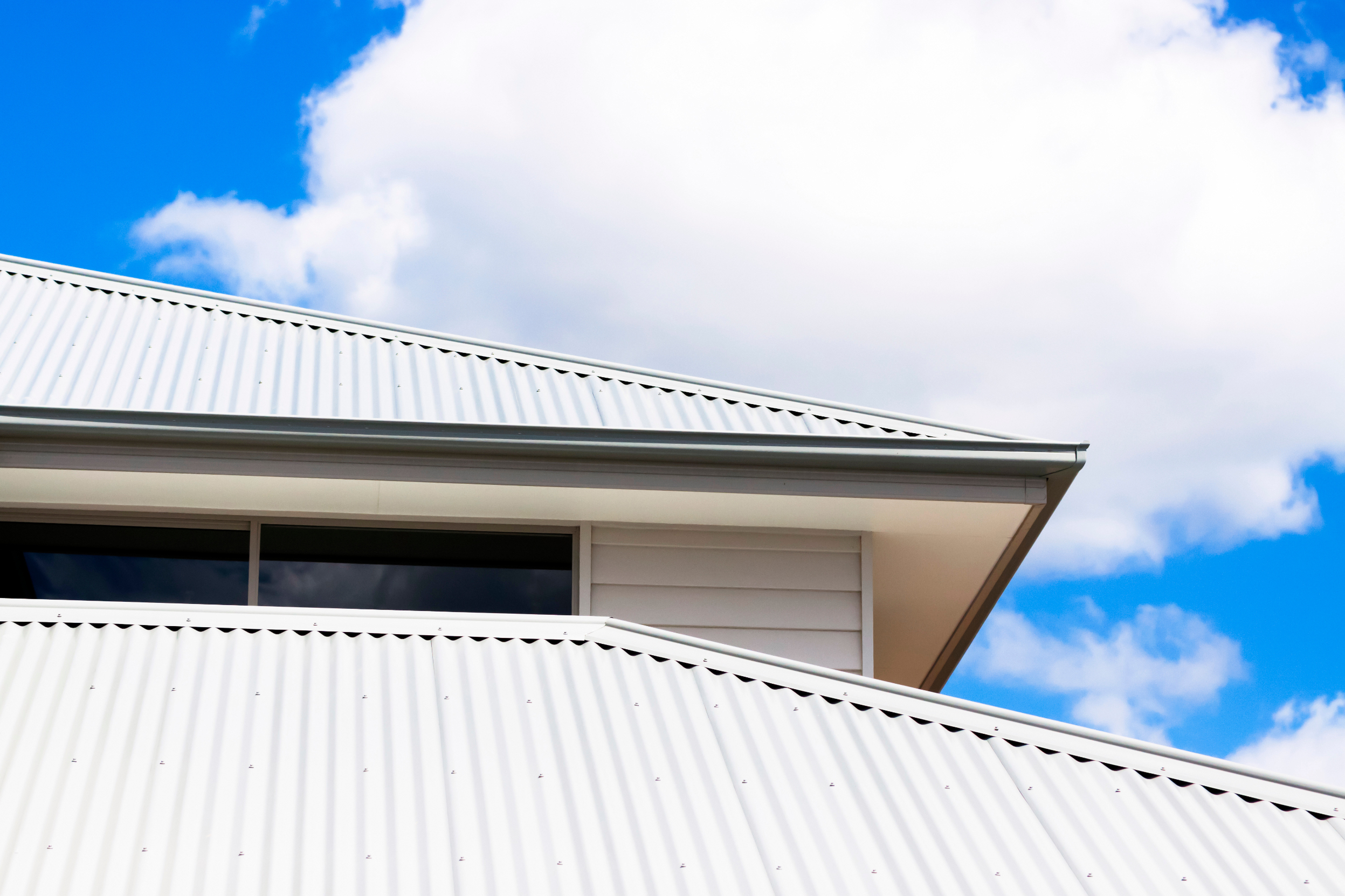 Closeup low angle view of corrugated iron roof of brand new house against blue sky with clouds, full frame horizontal composition with copy space