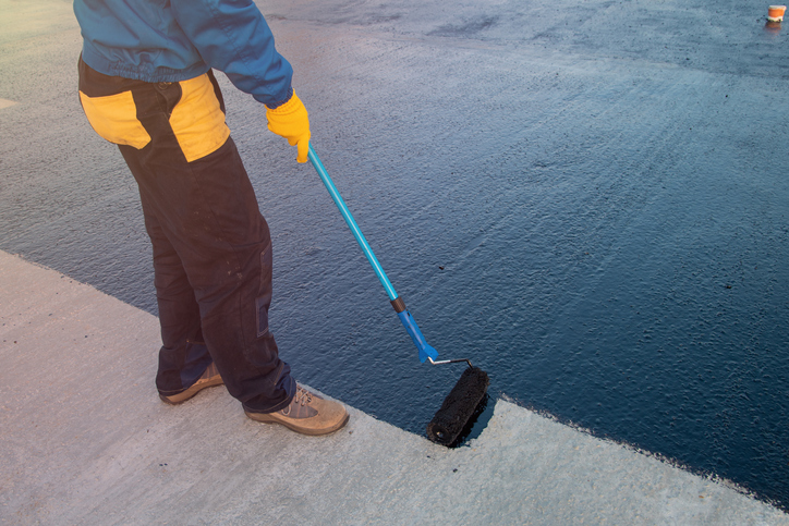 Roofer worker painting black coal tar or bitumen at concrete surface by the roller brush, A waterproofing. industrial worker on construction site laying sealant for waterproofing cement